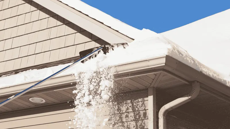Roof rake pulling packed snow off a residential roof edge to prevent an ice dam forming