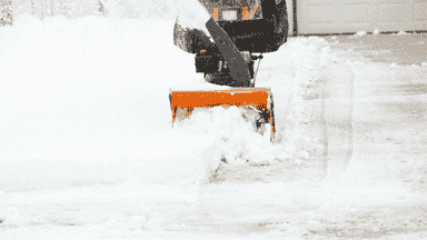 Snow blower clearing residential driveway for safe vehicle and walkway access.