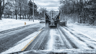 Truck spreading salt and de-icing material on roads to prevent ice buildup and improve safety.