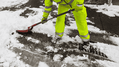Worker shoveling snow from sidewalk ensuring clean and safe walking paths during winter.